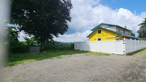 A yellow house with a green roof, surrounded by a white fence, located at the end of a gravel road. - The Seneca Sunsets Studio (Burdett)