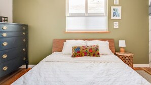 Une chambre à coucher avec un lit, une commode, une fenêtre et des œuvres d’art murales.