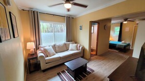 Ein Wohnzimmer mit einer Couch, einem Couchtisch, einem Deckenventilator und einem Fenster mit Vorhängen.