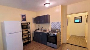 Eine kleine Küche mit Kühlschrank, Herd, Spüle und dunklen Holzschränken.
