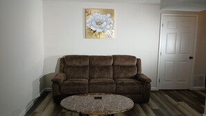 A living room with a brown sofa, a marble coffee table, and a wall-mounted painting.