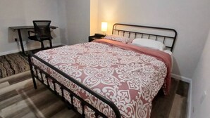 A bedroom with a bed, a chair, a nightstand, and a lamp.