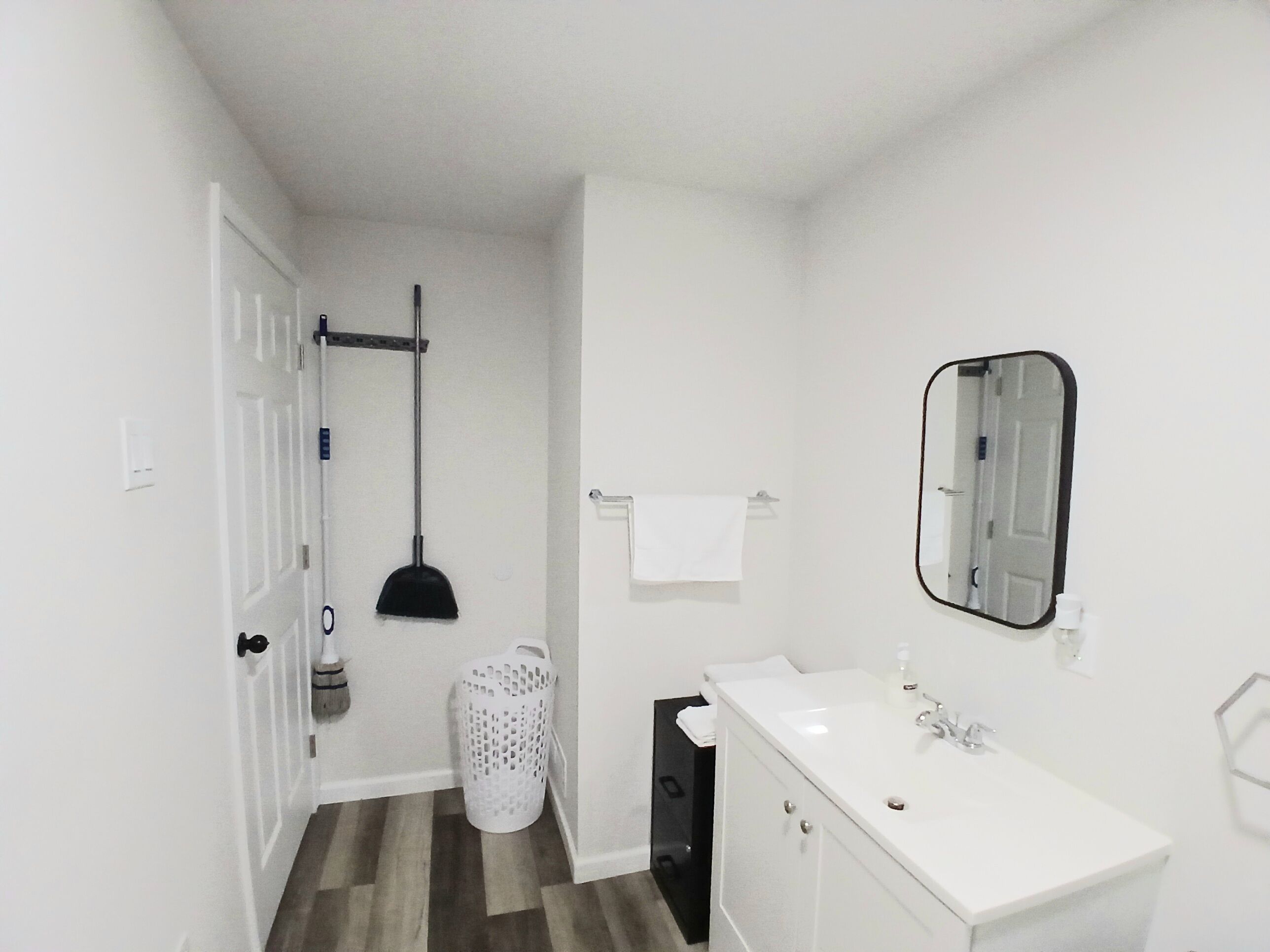 A bathroom with a white sink, a mirror, a broom, and a laundry basket.