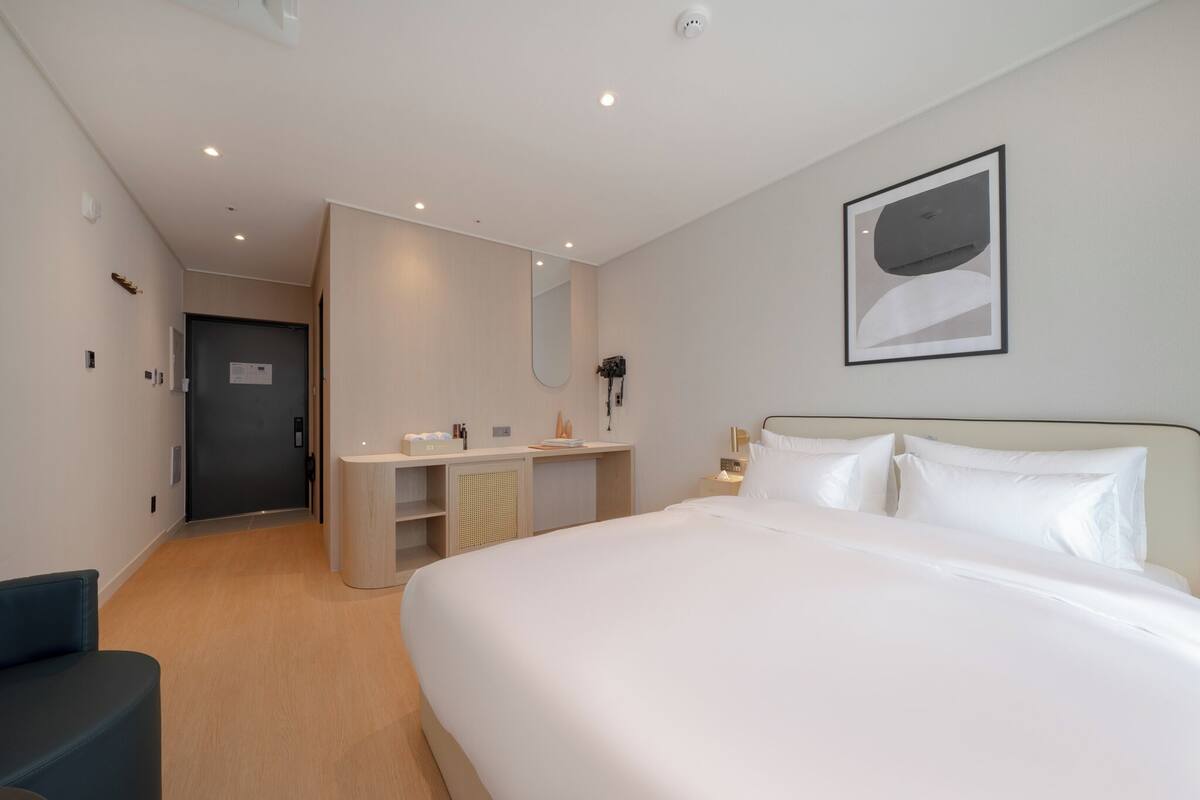 A modern hotel room with a large bed, a desk with a mirror, and a small seating area.