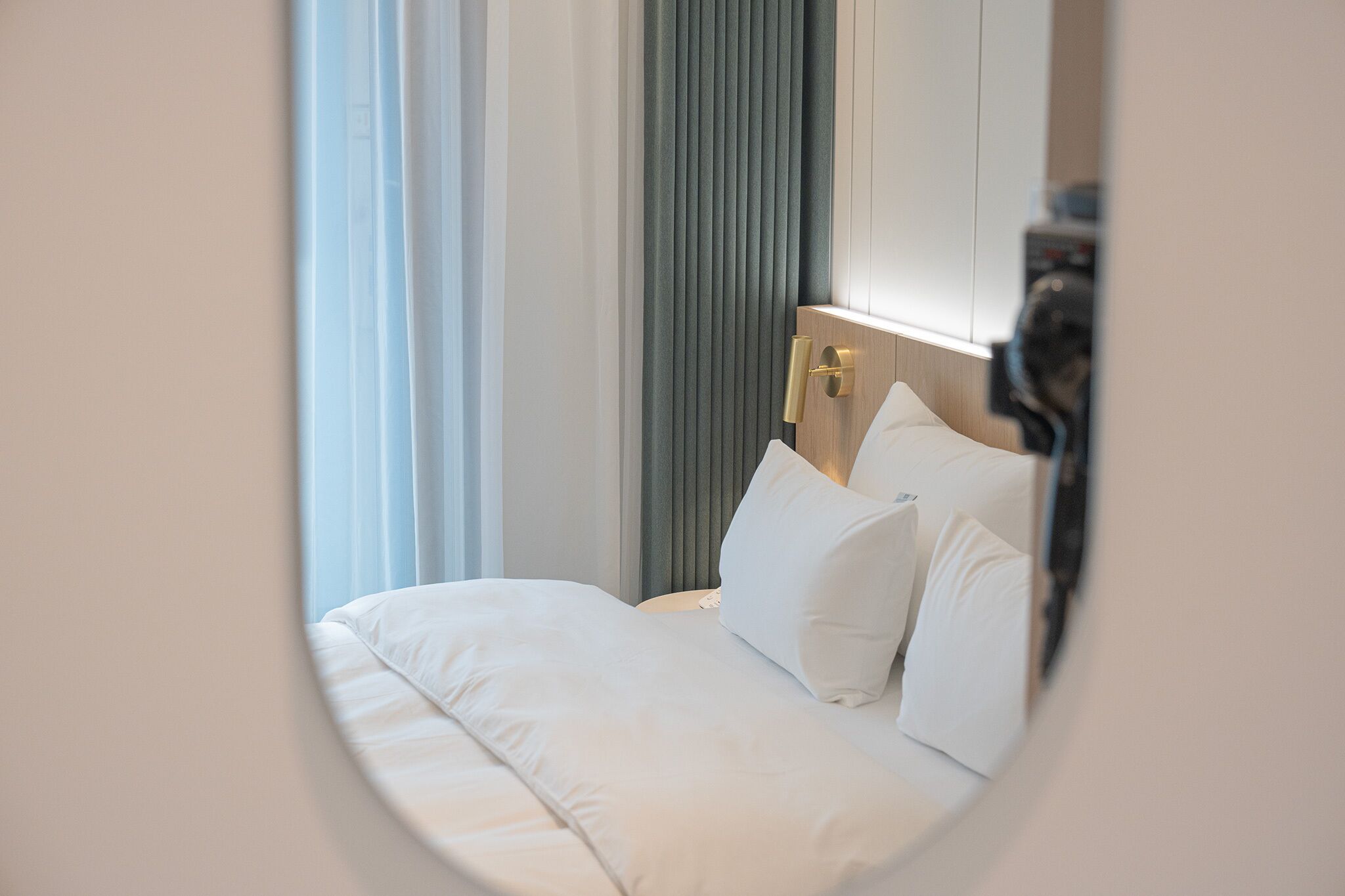 A neatly made bed with white linens and pillows, a wooden headboard, and a vertical panel with a light fixture.