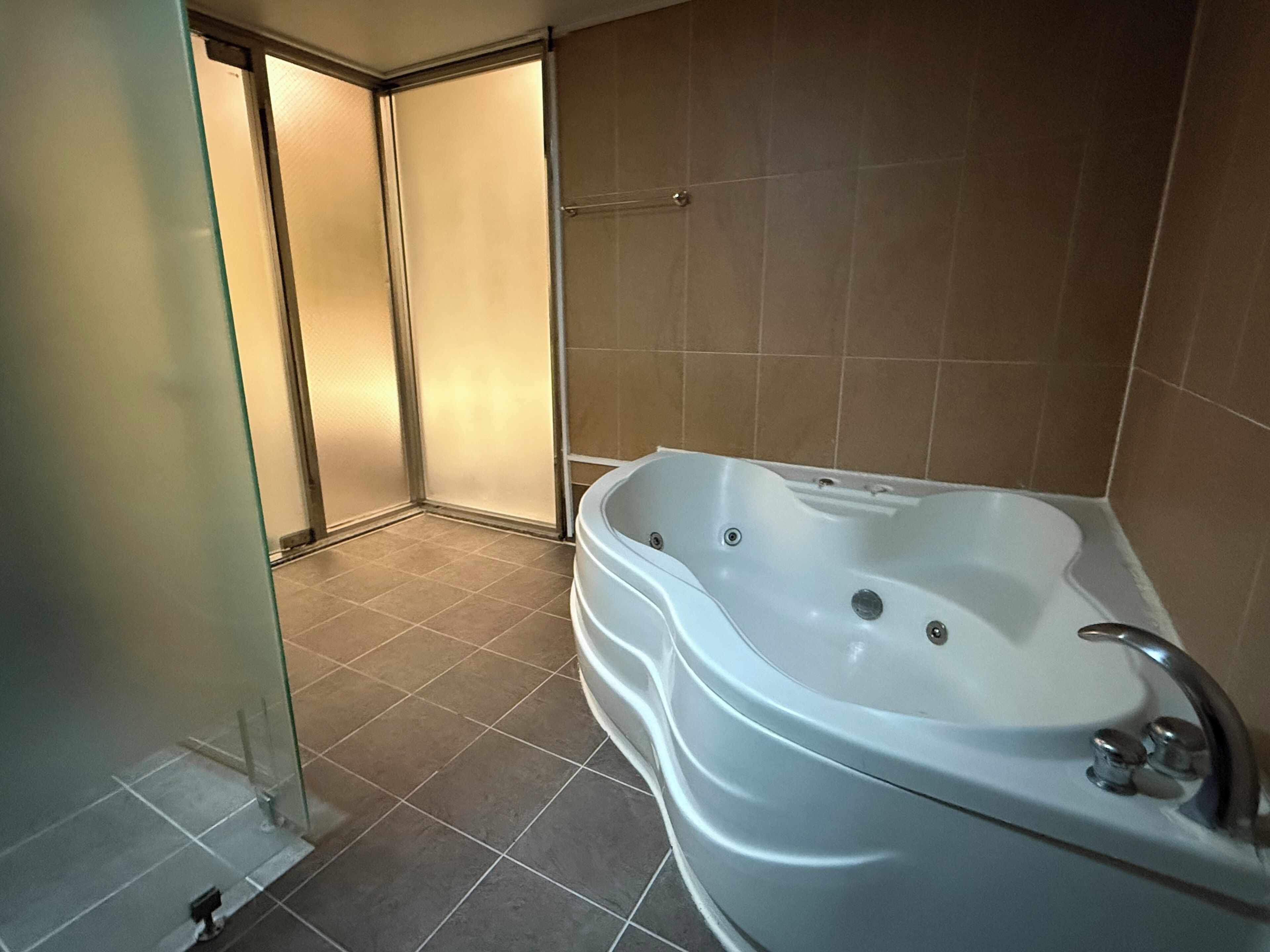 Un baño con una bañera grande, suelo de baldosas y cabina de ducha de vidrio.