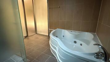 Un baño con una bañera grande, suelo de baldosas y cabina de ducha de vidrio.