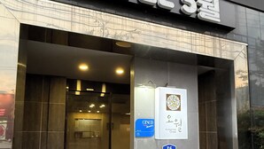 A hotel entrance with a glass door, a sign indicating the name 'HOTEL 5월', and a nearby sign for a nearby store.