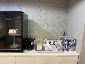 A kitchen with a refrigerator, coffee maker, and various food items.