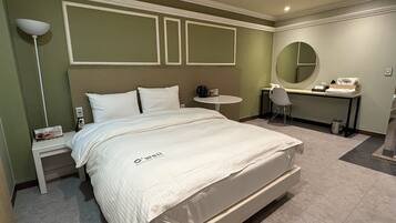 A hotel room with a bed, a desk, a chair, a round mirror, and a small table.