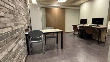 Un espacio de oficina moderno con pared de ladrillo, una pizarra, una mesa con sillas y dos escritorios de computadora con monitores.