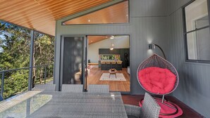 Un intérieur moderne comprenant un coin repas, un fauteuil suspendu rouge et une vue sur la cuisine grâce à une porte ouverte.