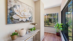 Un couloir orné d’une grande œuvre d’art florale, une console sur laquelle sont disposées des plantes, un lampadaire et une vue sur la verdure par une fenêtre.