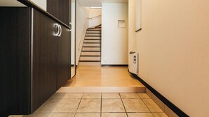 Um corredor estreito, com uma porta de madeira à esquerda, uma escada ao centro e um radiador à direita.