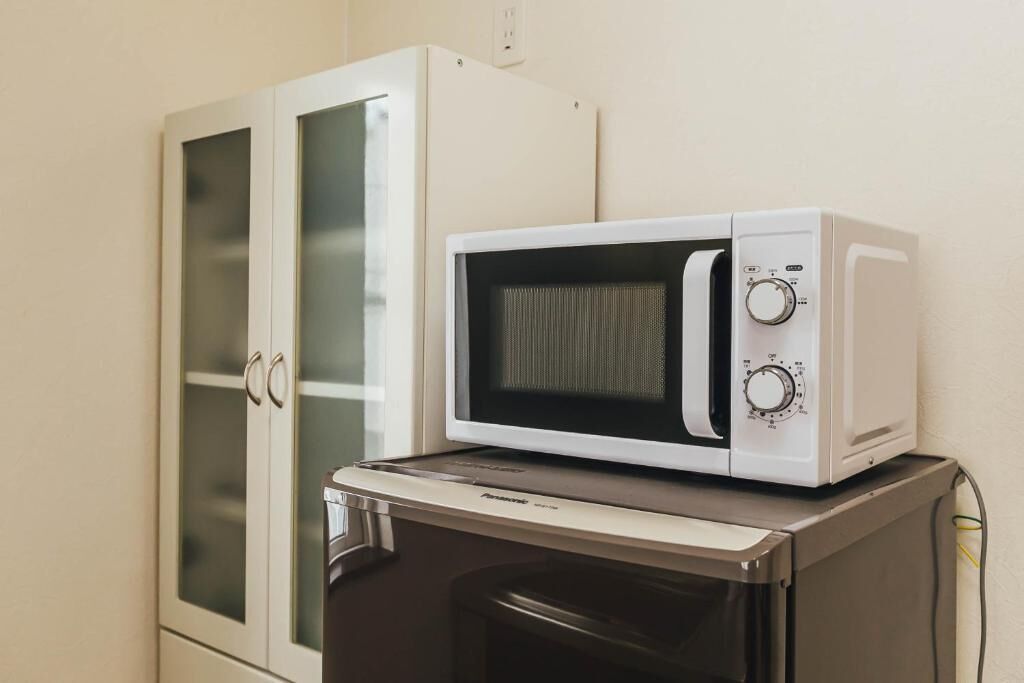 A microwave oven on top of a refrigerator, with a glass-fronted cabinet to the left.