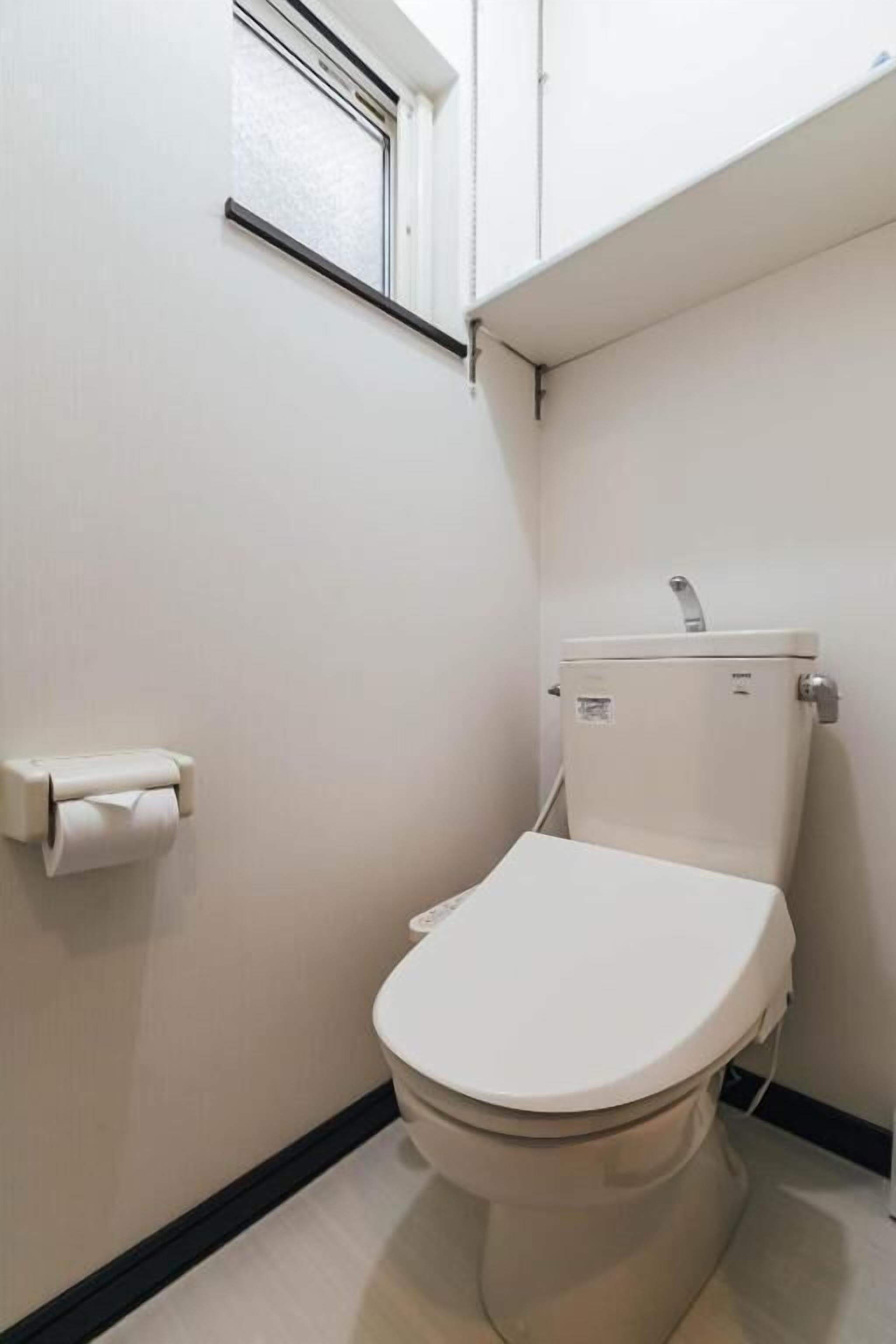Ein kleines, sauberes Badezimmer mit Toilette, Toilettenpapierhalter und einem Fenster über der Toilette.