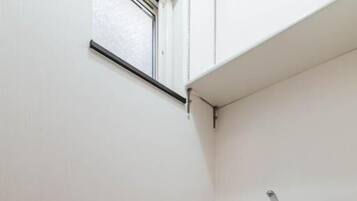 Ein kleines, sauberes Badezimmer mit Toilette, Toilettenpapierhalter und einem Fenster über der Toilette.