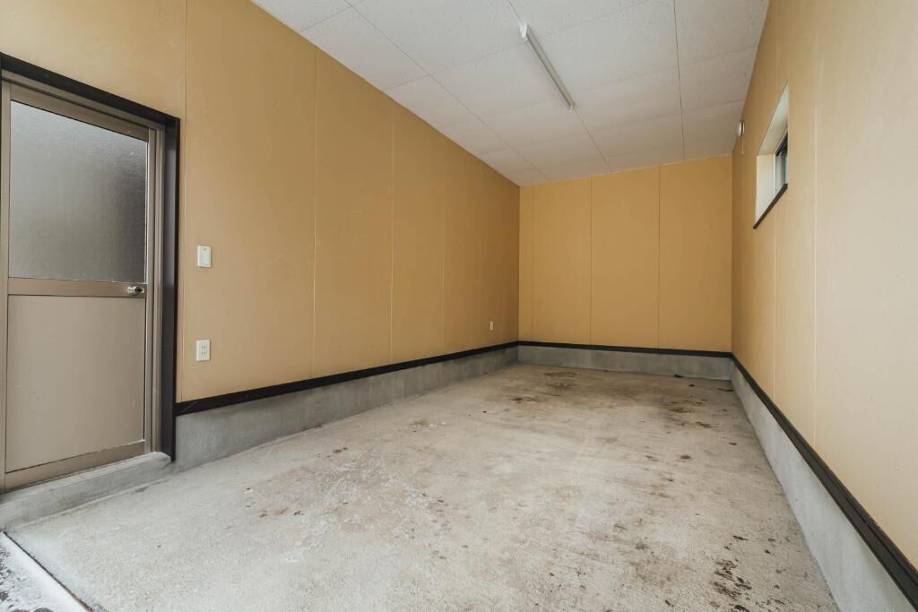 Un corridoio con pareti beige e pavimento in cemento, con una porta che include un pannello in vetro satinato e una piccola finestra sulla parete destra.
