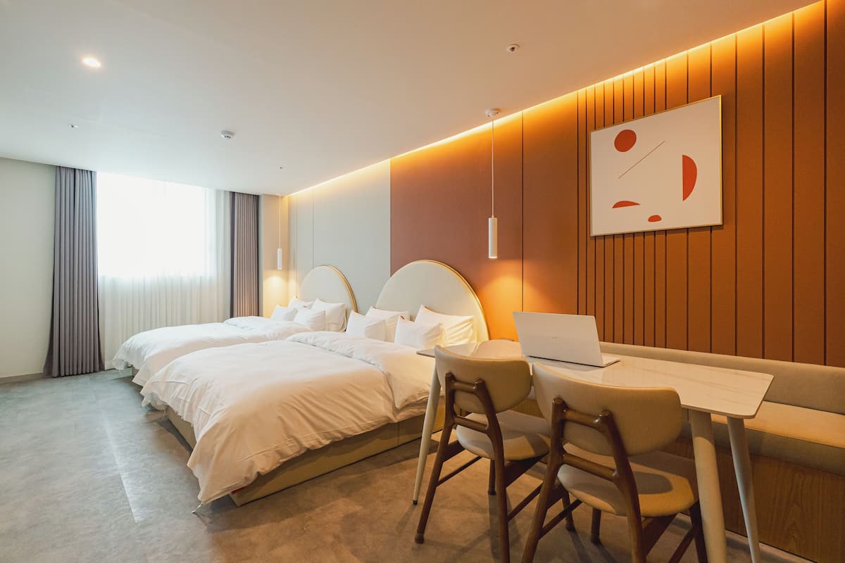 Habitación de hotel con dos camas, un escritorio con una computadora portátil y un cuadro abstracto grande en la pared.