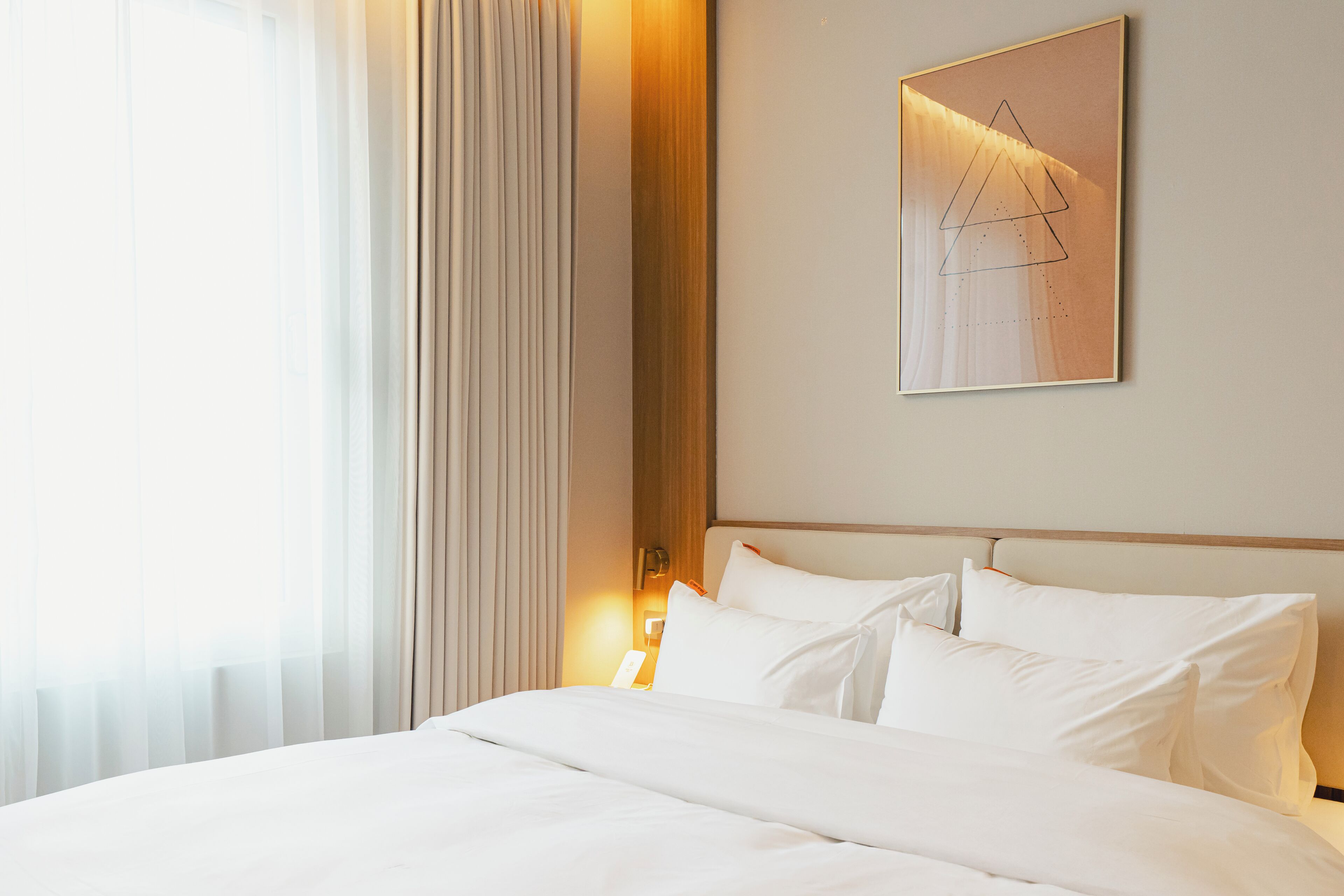Una camera d'albergo con un letto rifatto, un comodino con una lampada e un'opera d'arte appesa al muro.