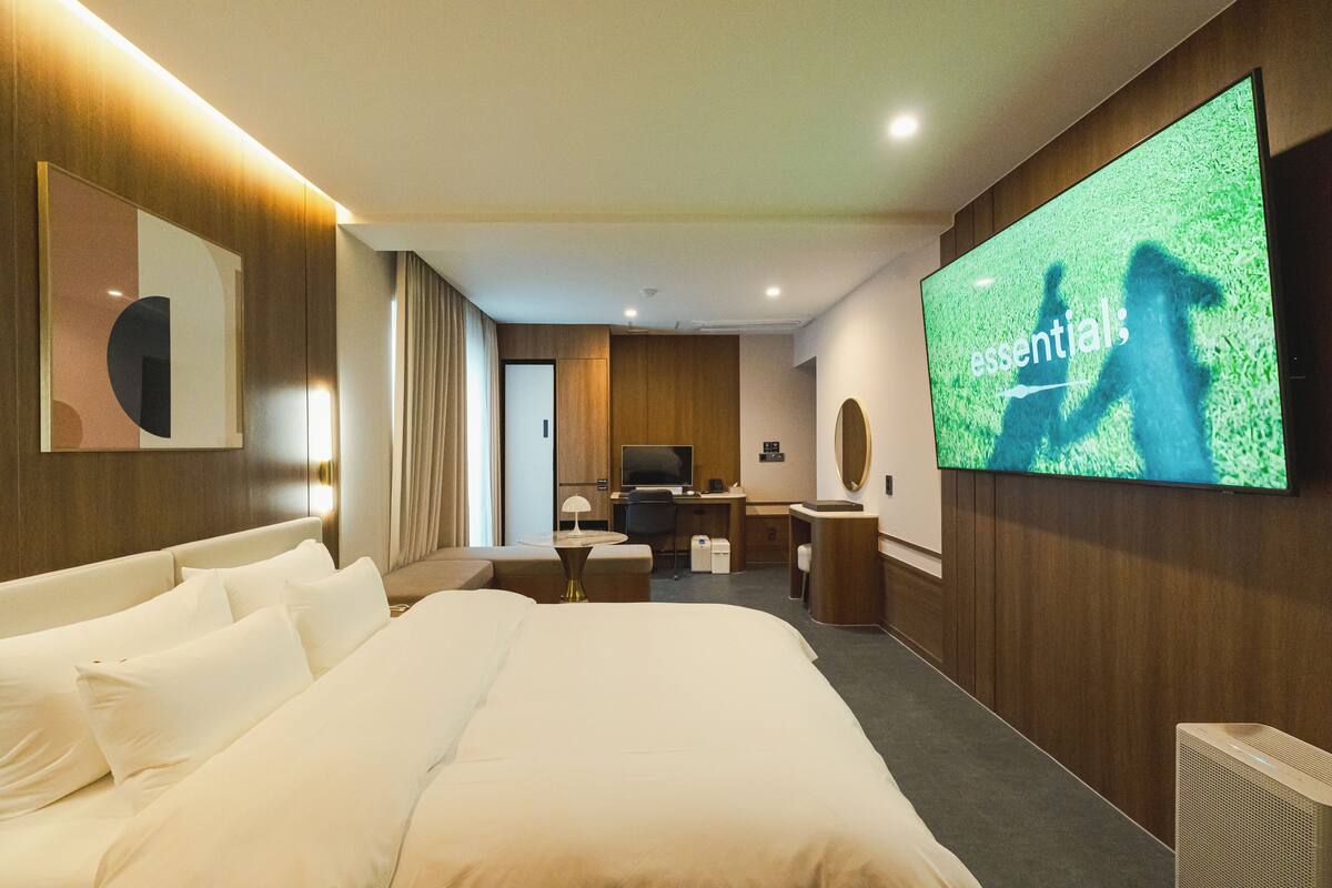 Habitación de hotel moderna con una cama grande, un escritorio, un televisor y un espejo grande en la pared.