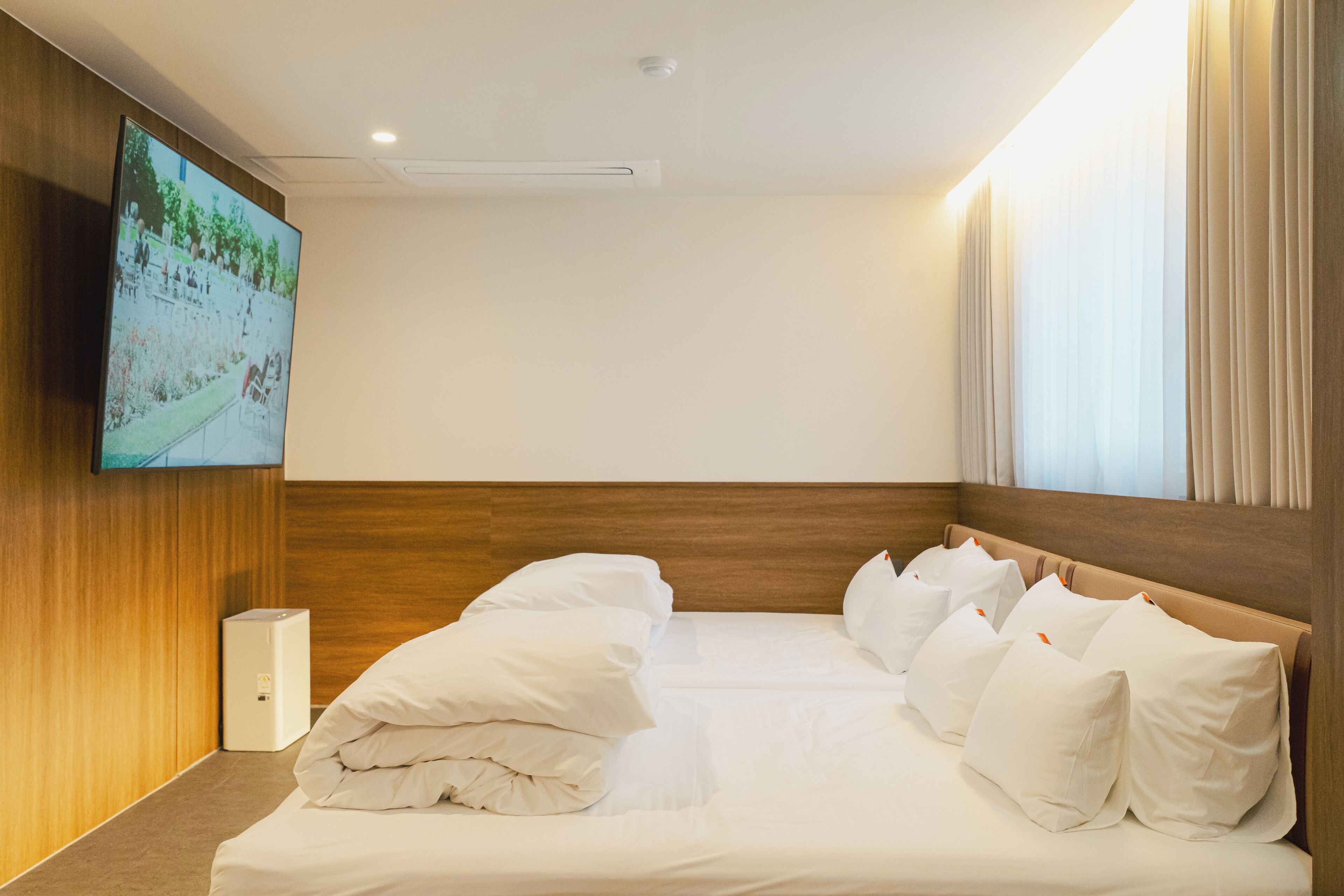 A hotel room with a wooden headboard, a flat-screen TV mounted on the wall, and a bed with white linens and pillows.