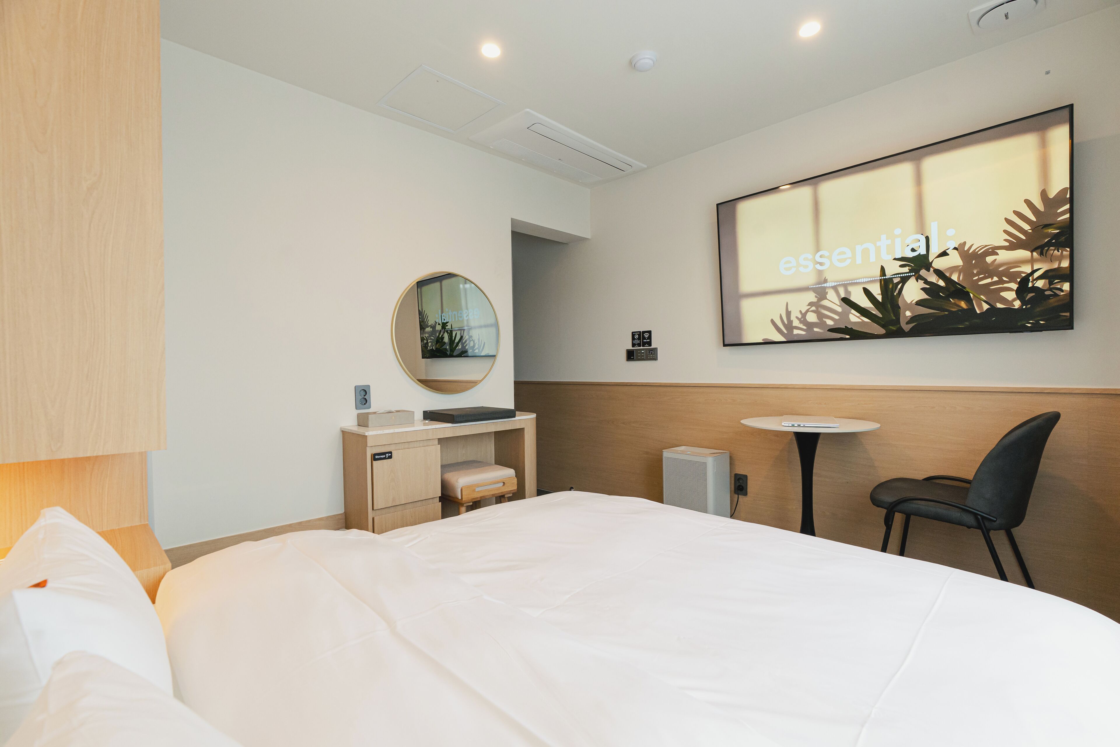 Una habitación de hotel moderna con una cama grande, un escritorio pequeño, un espejo redondo, una mesa redonda y una silla.