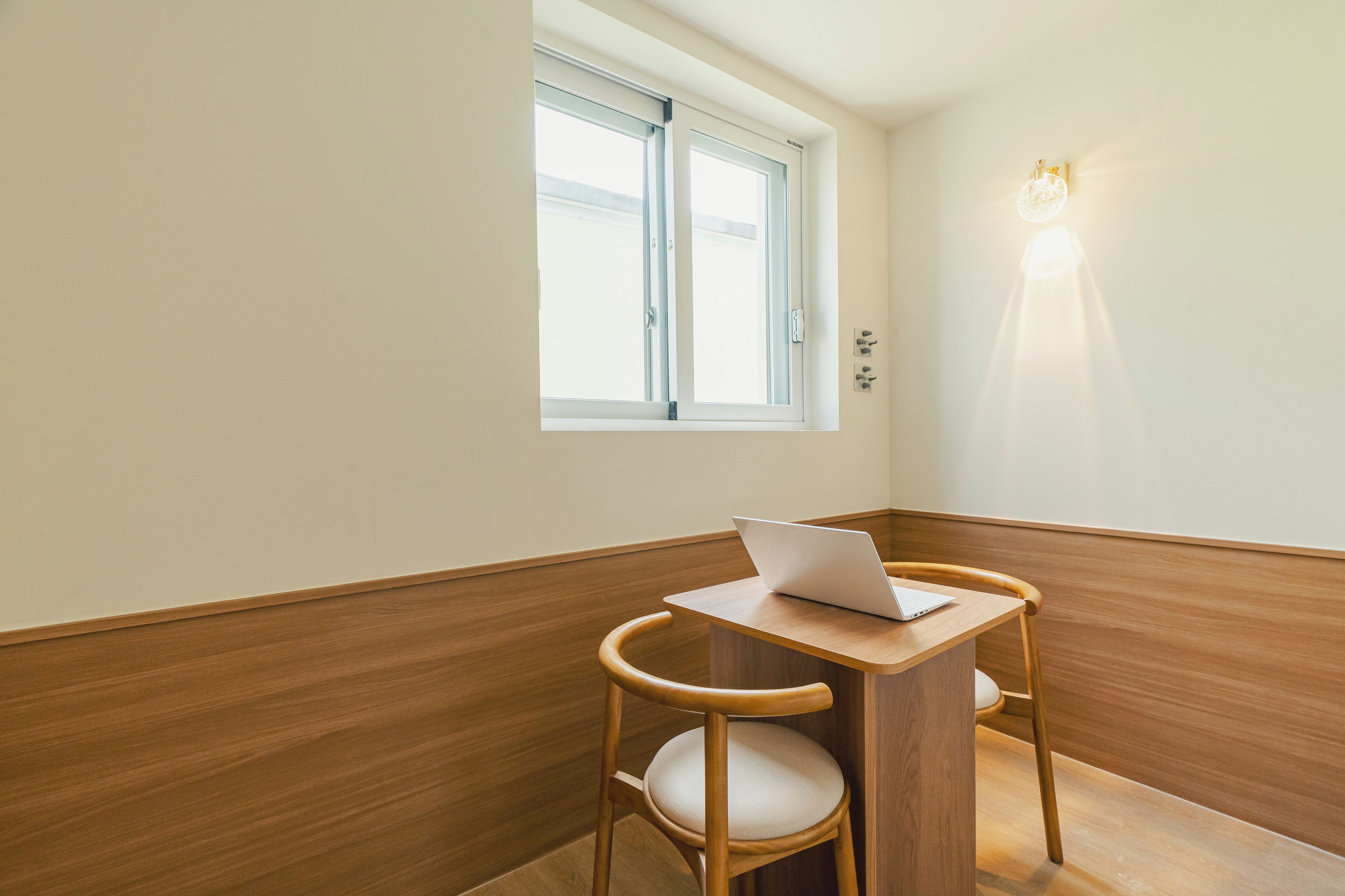 A small room with a wooden desk and chair, a laptop, and a window with blinds.