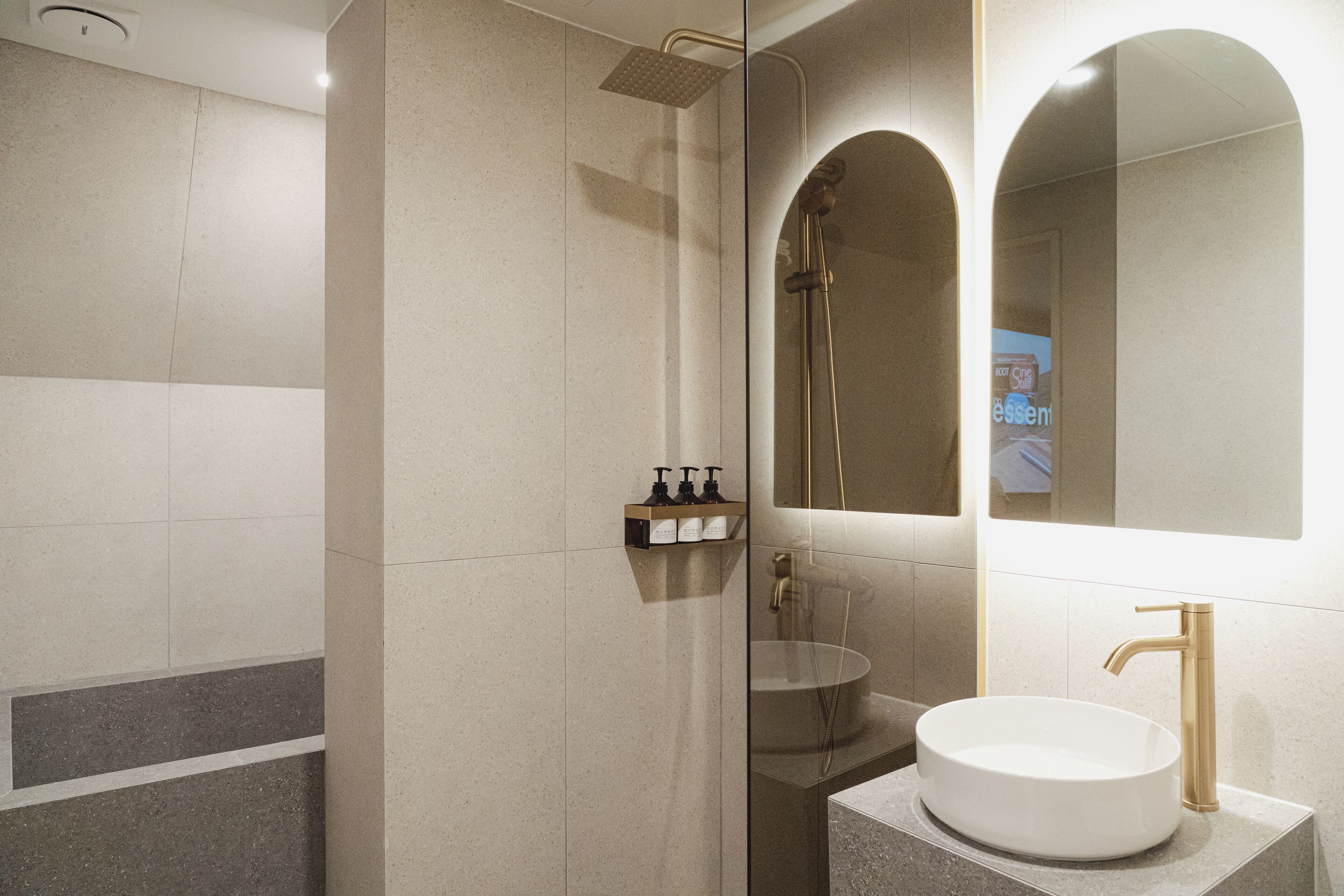 A modern bathroom with a glass-enclosed shower, a round sink, and a large mirror.