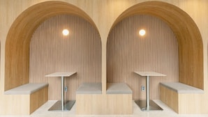 Un baño moderno con dos lavamanos bajo arcos de madera, cada uno con un pequeño banco y un espejo.