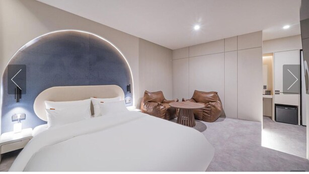 Una habitación de hotel moderna con una cama grande, una zona de estar con sillones de cuero y una pequeña mesa.