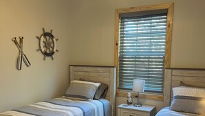 A bedroom with two beds, a ceiling fan, a ship's wheel decoration, and a window with blinds.