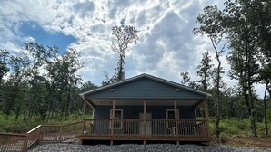 A cabin with a porch, surrounded by trees and gravel.