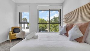 Un dormitorio moderno con una cama grande, un sillón amarillo y vistas a árboles a través de amplias ventanas.