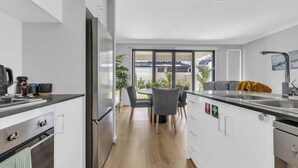 Una cocina moderna con una isla central, un comedor con sillas y vistas al exterior a través de grandes ventanales.