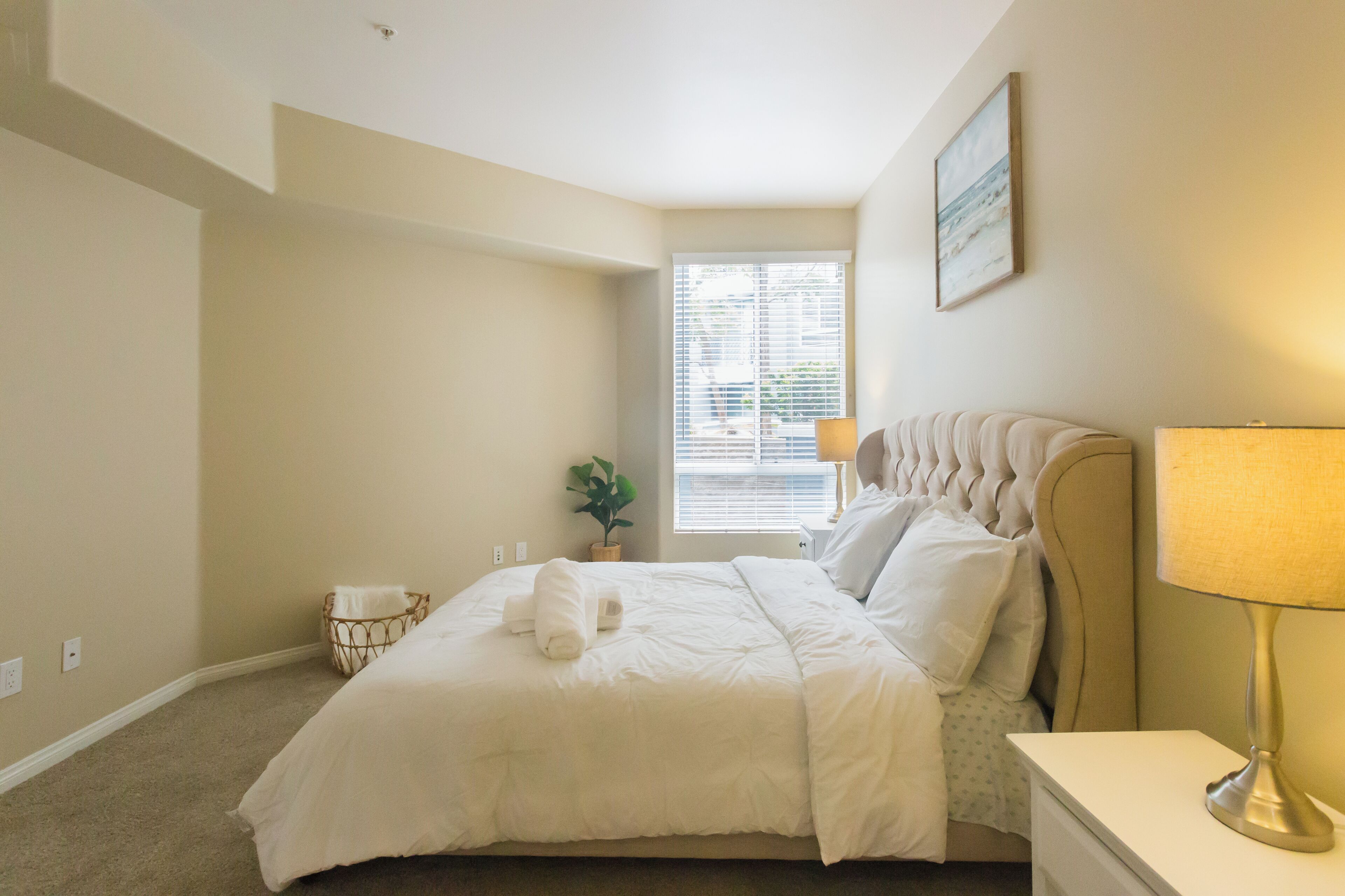 Een net opgemaakt bed met witte lakens, een bedlampje en een kleine kamerplant op het nachtkastje.