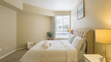Een net opgemaakt bed met witte lakens, een bedlampje en een kleine kamerplant op het nachtkastje.