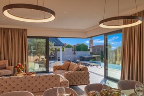 Een moderne woonkamer met een grote glazen deur die uitkomt op een terras, een zwembad en uitzicht op een historisch gebouw.