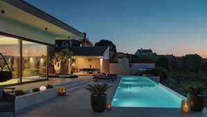 Ein moderner Poolbereich im Freien mit einer gläsernen Veranda, Lounge-Möbeln und Topfpflanzen.