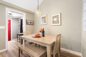 Uma sala de jantar com mesa de madeira, cadeiras, um banco, um lustre e quadros nas paredes.