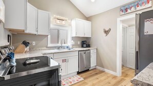 Una cocina moderna con armarios blancos, un refrigerador de acero inoxidable y una cafetera.