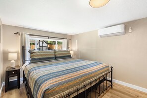 A bedroom with a bed, a nightstand, a window with curtains, and an air conditioning unit on the wall.