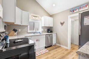 A modern kitchen with white cabinets, a stainless steel dishwasher, and a coffee maker.