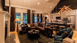Een ruime woonkamer met een grote hoekbank, een salontafel en een open haard. Er is een keuken met moderne apparatuur en een eethoek.