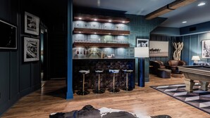 Een barruimte met houten planken, barstoelen en een pooltafel in een modern interieur met blauwe muren en houten vloeren.