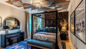Een slaapkamer met een hemelbed, een bureau met een stoel, een spiegel en een groot raam.
