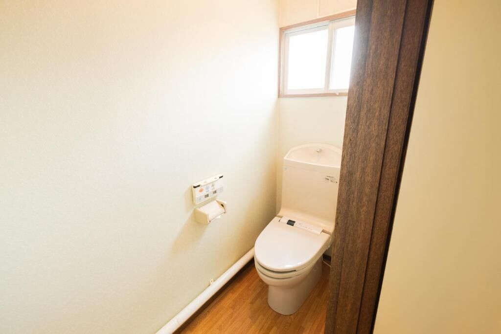 Un baño pequeño y limpio con inodoro, soporte para papel higiénico y una ventana sobre el inodoro.
