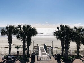 Blick auf einen Strand mit Palmen, einer Holzterrasse und einer Geländer.
