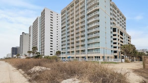 Un hotel frente al mar con varios pisos, balcones y una zona de playa arenosa.