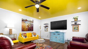 A living room with a yellow sofa, red leather chairs, a blue cabinet, a flat-screen TV, and a ceiling fan.